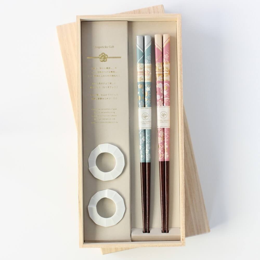 Set of blue and pink chopsticks and a pair of ring shaped chopstick rests in a wooden box