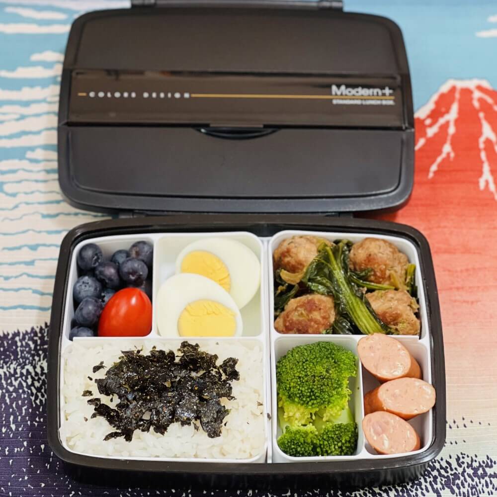 Black bento box with compartments of food on a colorful background