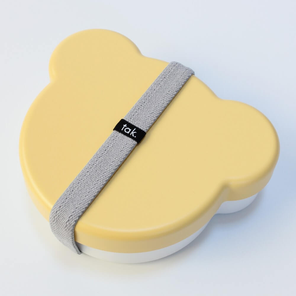 Yellow bear face shaped bento box with a gray strap and 'tak' branding on a white background