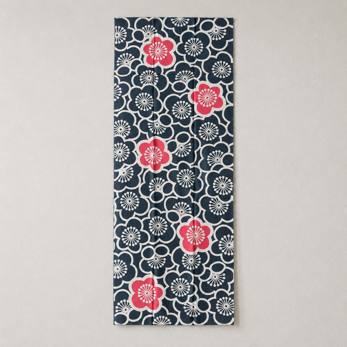 A vertical rectangular tenugui fabric featuring a navy blue background with a Japanese plum blossoms adorning the entirety of the fabric as a pattern, accented by four bright pink blossoms.