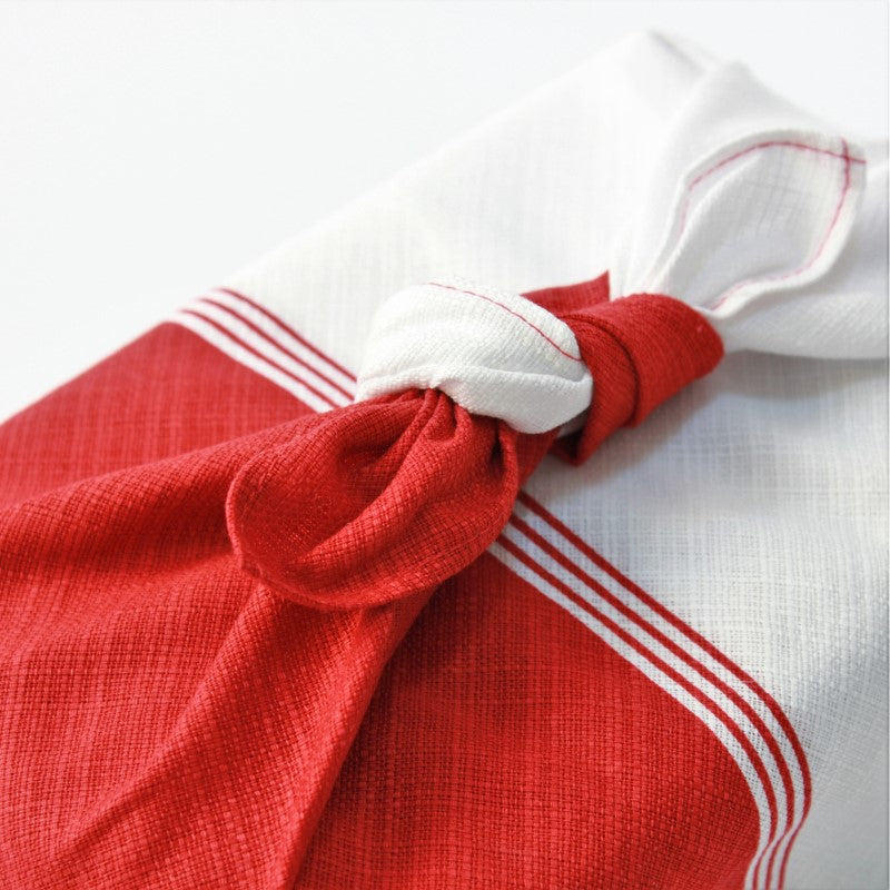 Close up photo showing the knot of a wrapped red white furoshiki around a bento box