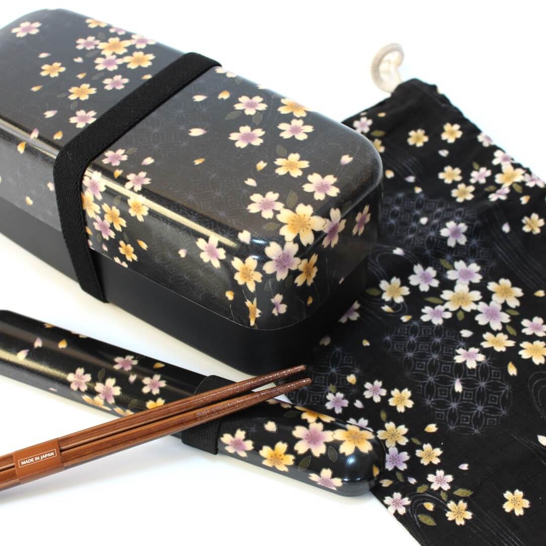 black Japanese bento box with sakura patterns, with chopsticks and a black bento bag on a white background
