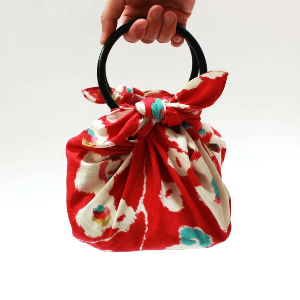 Red fabric bag with white patterns held by a hand against a white background