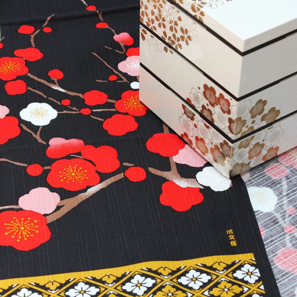 white picnic bento box on the corner of crane dance furoshiki showing red plum flowers