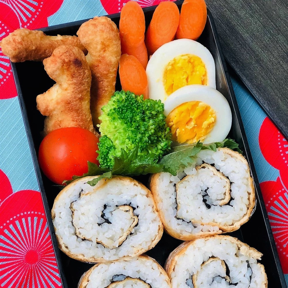 Overhead view of bento box containing sushi rolls, chicken nuggets, veges and boiled egg