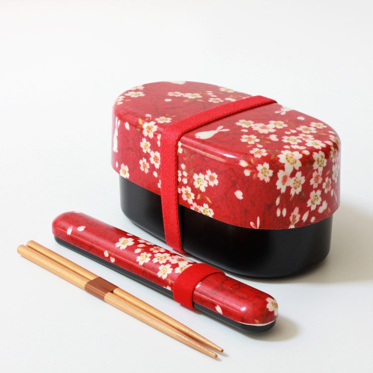 red bento box with sakura and rabbit patterns next to a chopsticks case and chopsticks